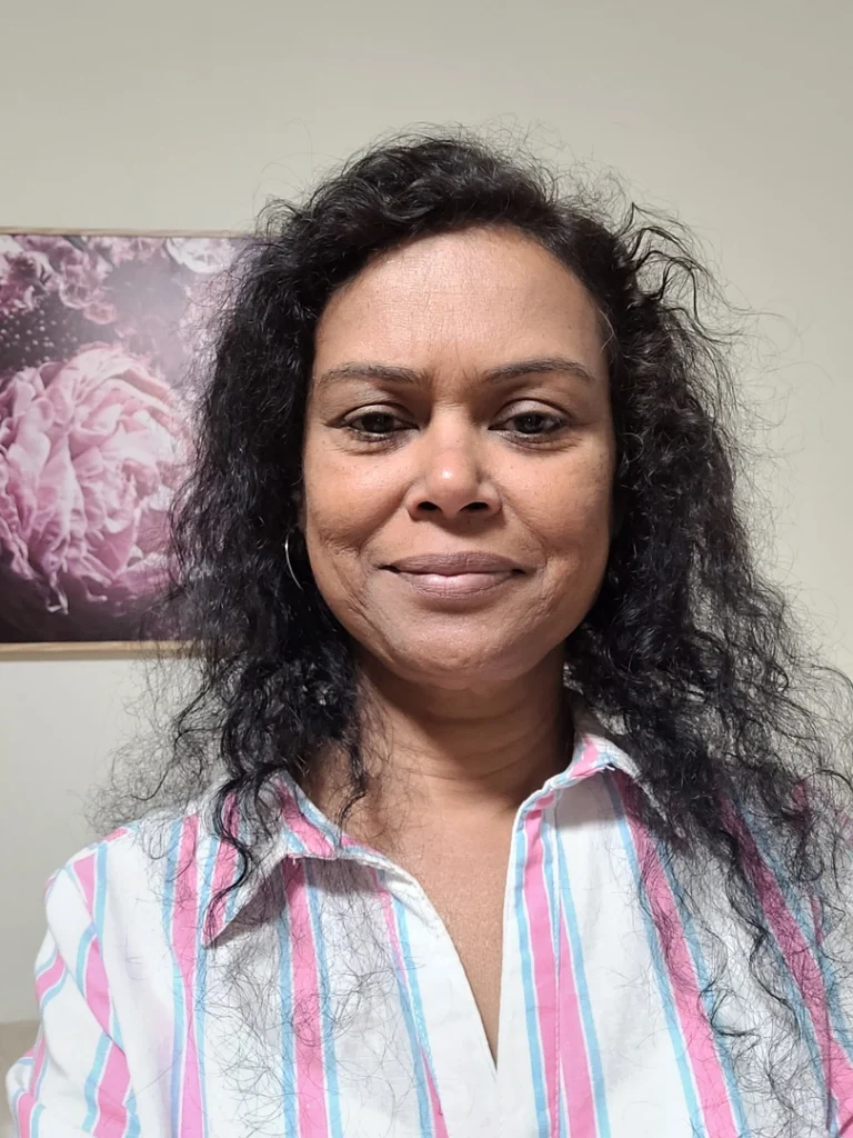 Woman smiling in striped shirt near floral painting.