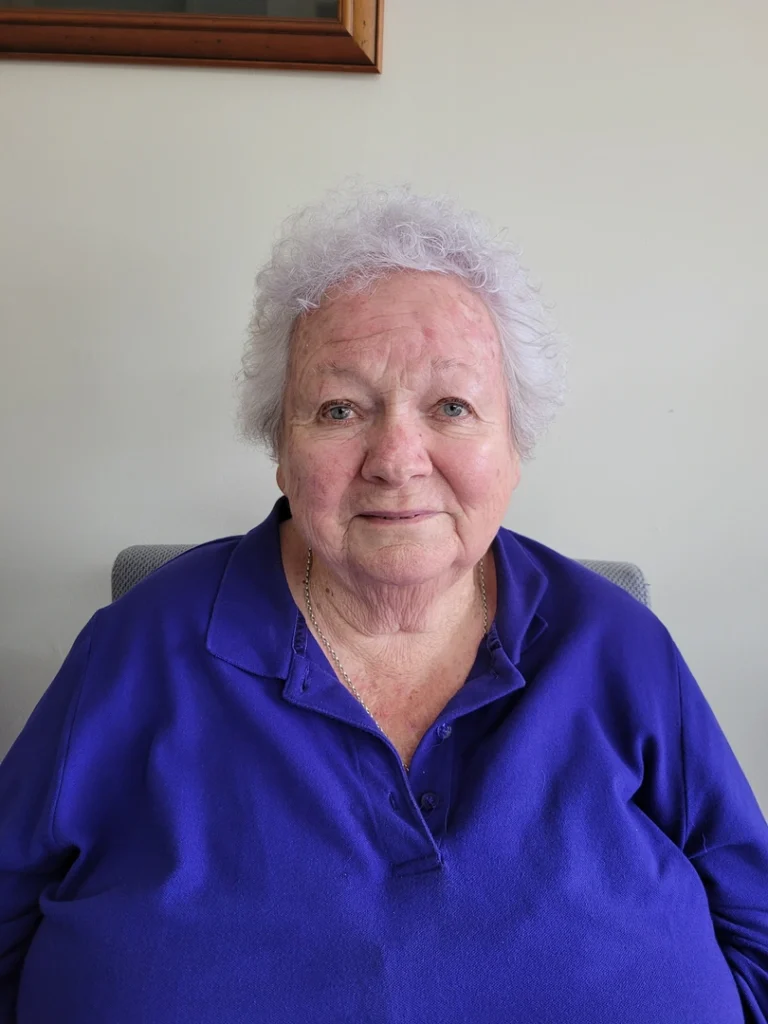 Elderly woman smiling in blue shirt.