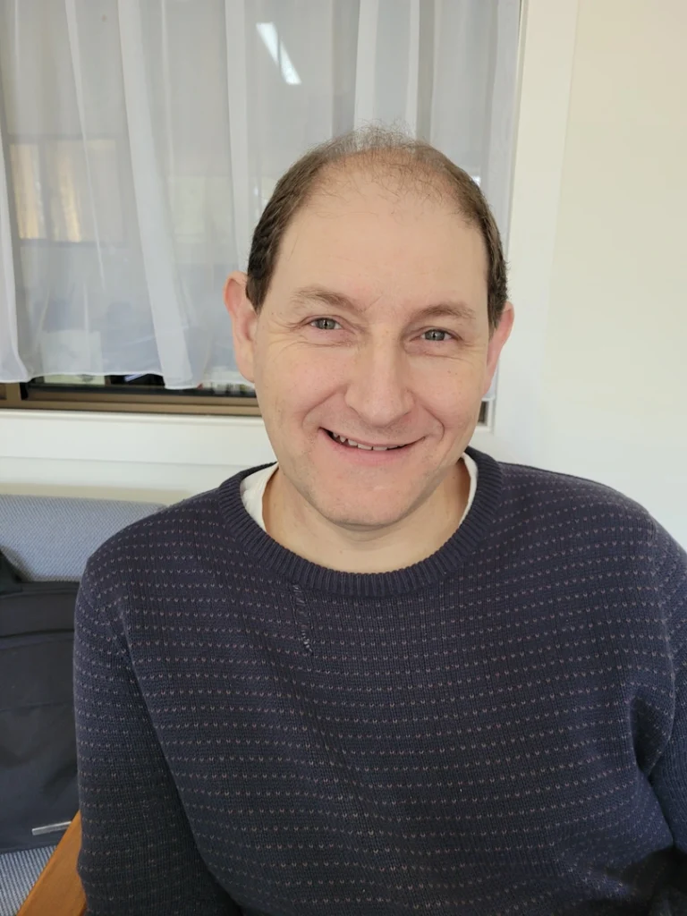 Man smiling indoors, wearing a dark sweater.